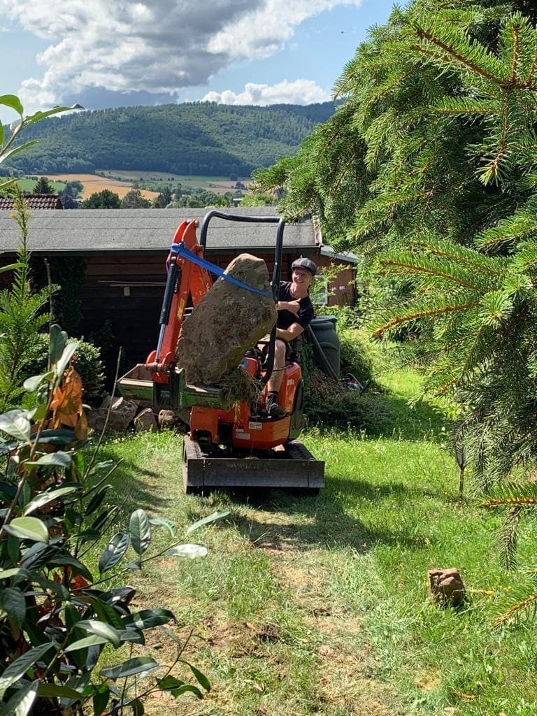 Minibagger versetzt einen massiven Felsbrocken bei Erdarbeiten im Garten