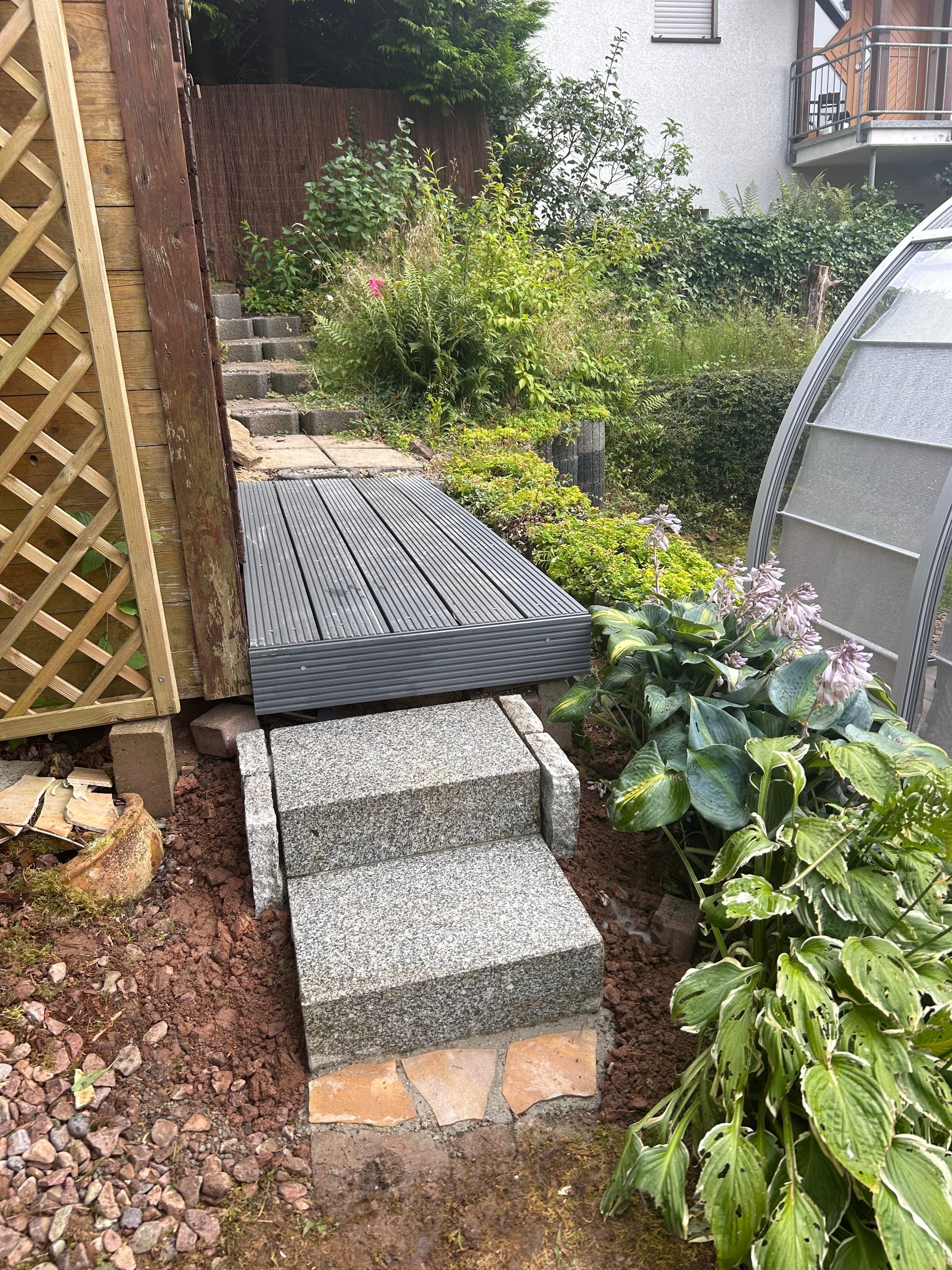 Neue WPC-Terrassendiele mit sauberer Granitkante und Hosta-Bepflanzung