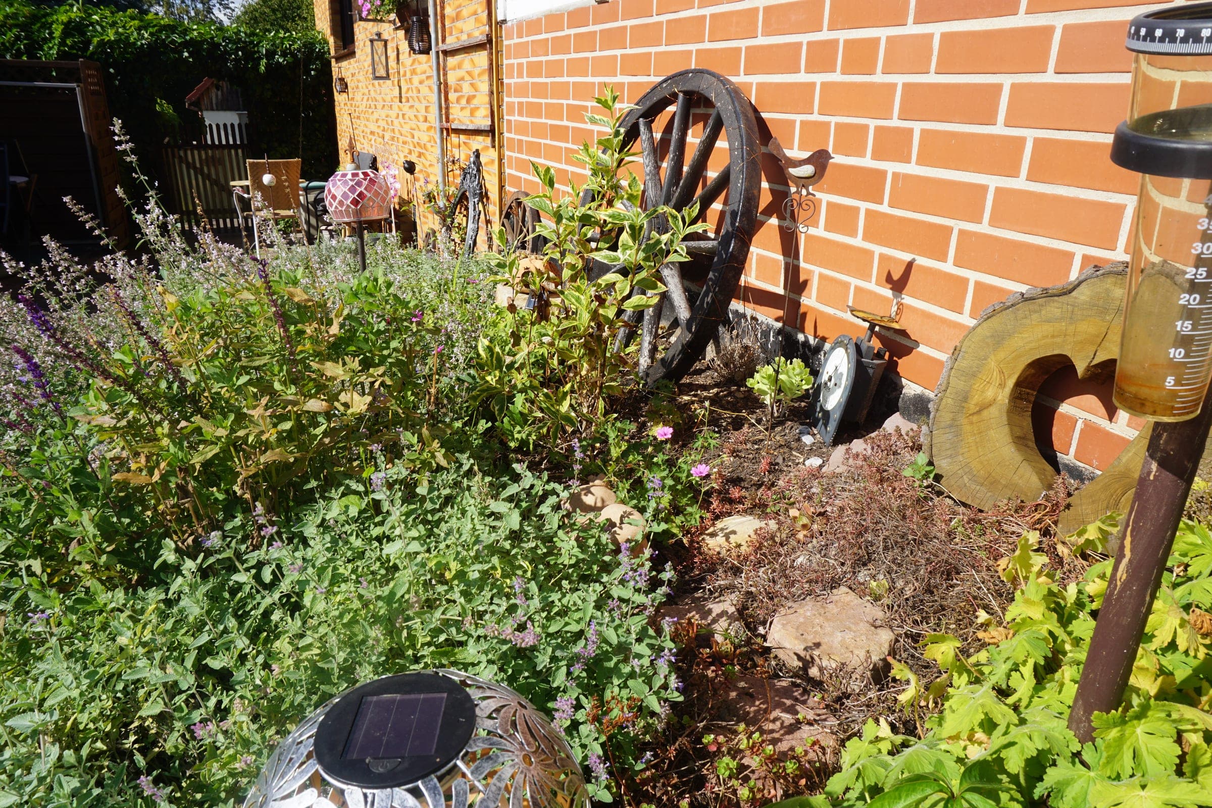 Staudenbeet mit Lavendel und altem Wagenrad vor einer Klinkerwand